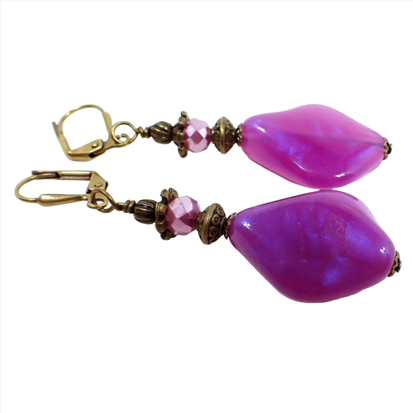 Front view of the handmade color shift purple lucite earrings. The metal is antiqued brass in color. There are pearly glass faceted beads at the top and angled teardrop beads at the bottom. The bottom beads have an indented curve and are bright purple in color with hints of sparkly purple as you move around.