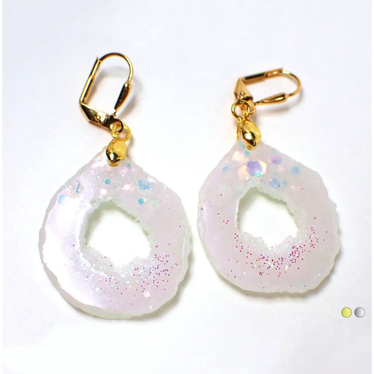 Enlarged front view of the gold tone plated handmade resin druzy geode style earrings. They are a rounded teardrop like shape with irregular edge and an open middle area with a druzy like texture. The resin is iridescent pearly white. There is chunky iridescent glitter at the top and tiny pink iridescent glitter at the bottom.