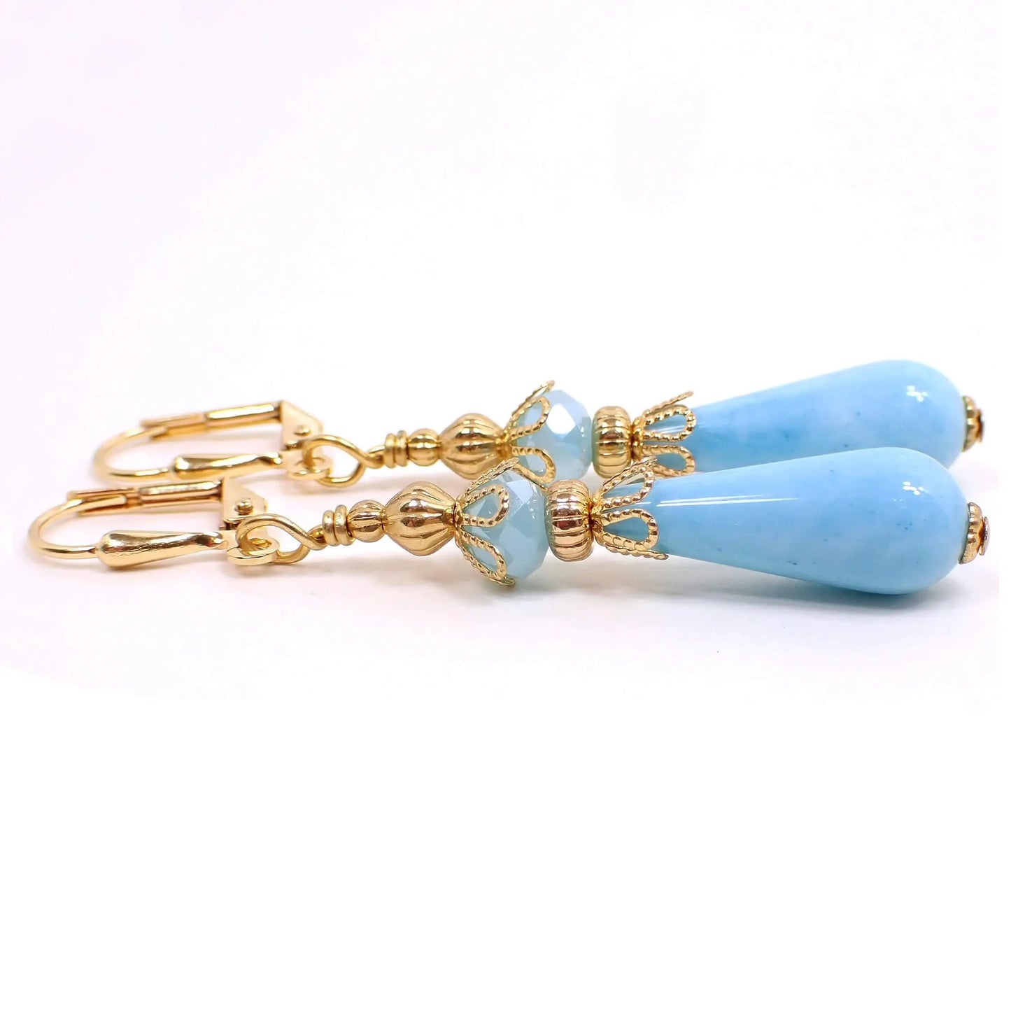 Side view of the handmade small teardrop earrings with vintage lucite beads. The metal is gold plated in color. There is a light blue faceted glass crystal bead at the top. The bottom bead is a light blue teardrop shaped lucite bead.