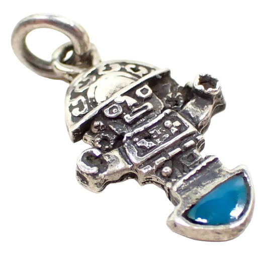 Enlarged angled view of the front of the small Incan Deity charm. It is antiqued silver tone in color and is shaped like Inti the Sun God. There is a small turquoise gemstone cab at the bottom of the charm and a silver tone jump ring attached to the top.