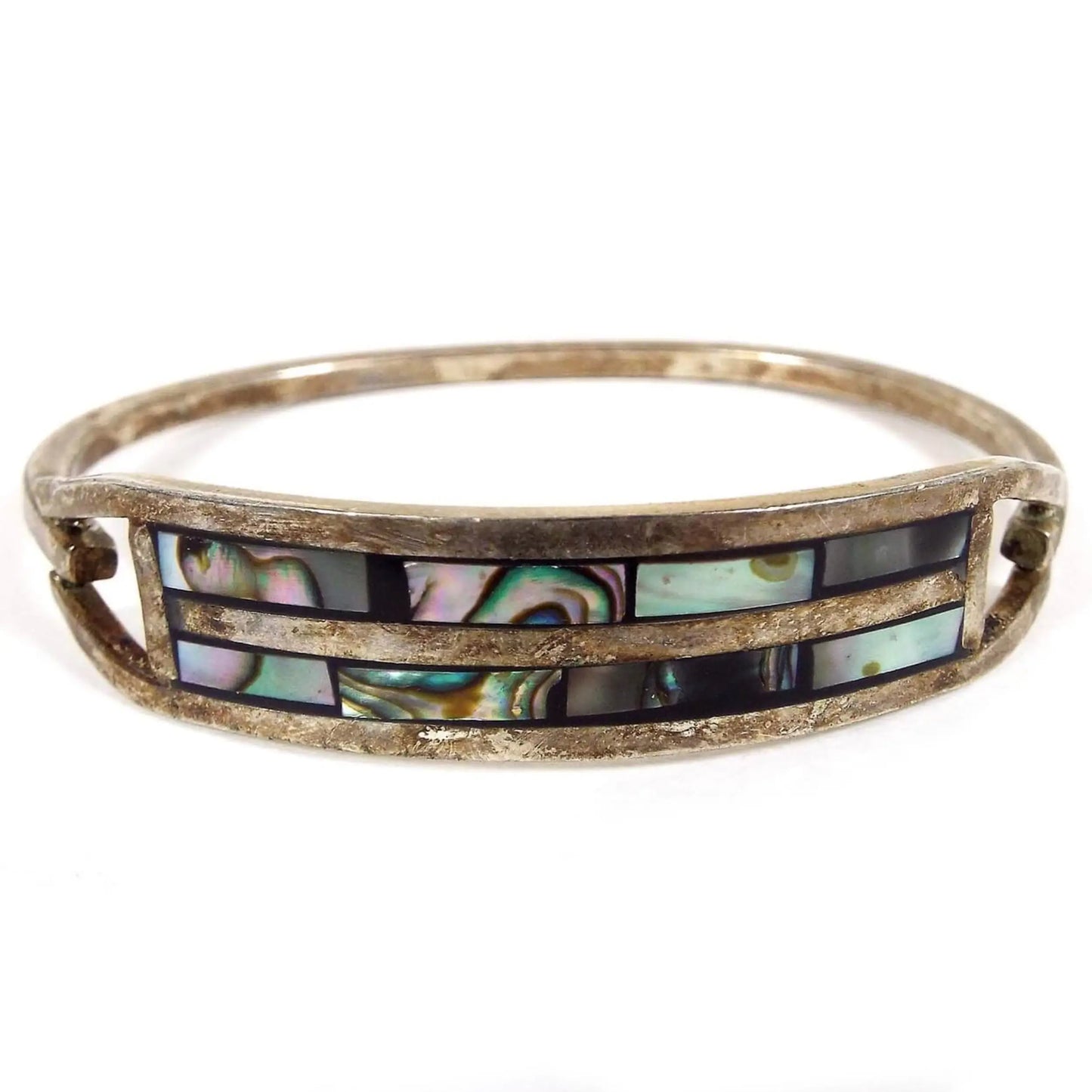 Front view of the retro vintage Taxco hinged bangle bracelet. It has darkened silver tone color metal. The front has a curved bar area with two rows of pearly multi color inlaid abalone shell.