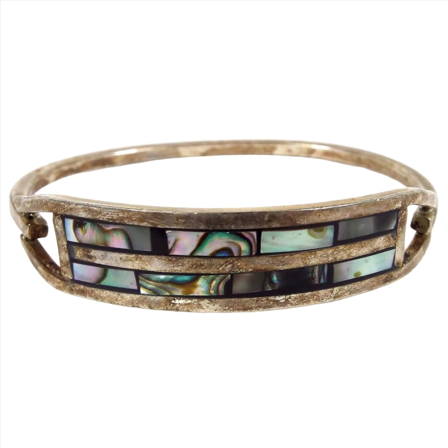 Front view of the retro vintage Taxco hinged bangle bracelet. It has darkened silver tone color metal. The front has a curved bar area with two rows of pearly multi color inlaid abalone shell.