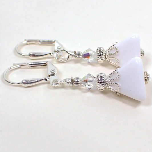 Side view of the small handmade pyramid earrings. The metal is silver plated in color. There are small faceted glass AB clear beads at the top of the earrings. The bottom beads are vintage lucite, are white in color, and are triangle pyramid shaped.