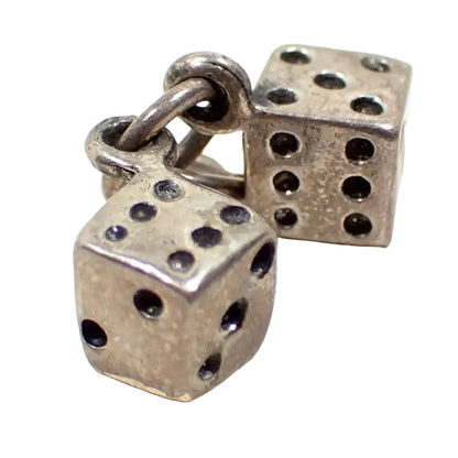 Enlarged view of the tiny miniature dice charm. There are two separate six sided dice made of pewter. They are square in shape, but not perfectly square. The color is light gray with black indented dots for the markings. Each one has a small loop that is joined by a jump ring so you can attach it to your charm bracelet.