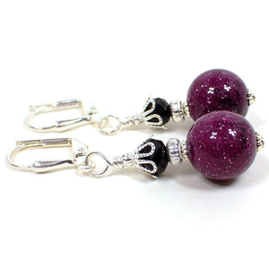 Side view of the handmade galaxy earrings. The metal is silver plated in color. There are black glass faceted beads at the top. The bottom beads are vintage lucite and are purple with specks of white, black, and glitter for a galaxy like appearance.