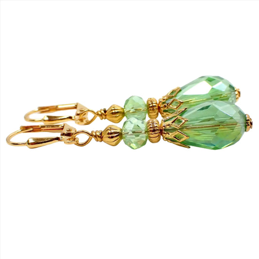Side view of the vintage style handmade faceted glass crystal teardrop earrings. The metal is gold plated in color. The beads are a light AB green. 