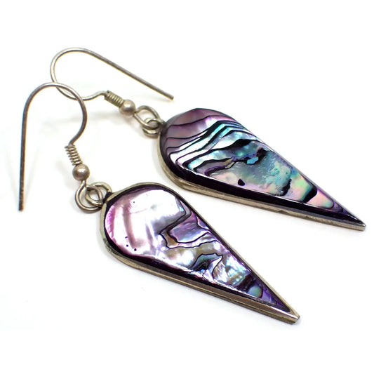 Enlarged angled view of the retro vintage Mexican alpaca earrings. The metal is silver tone in color. They are shaped like upside down teardrops. The fronts are abalone shell with multi color areas that are pearly and flash as you move around in the light.