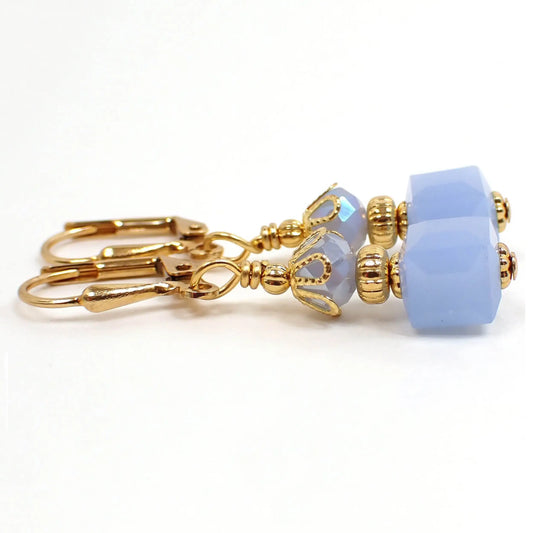 Side view of the small glass beaded earrings. The metal is gold plated in color. There are faceted glass crystal rondelle beads at the top and small cube shaped glass beads at the bottom. The beads are light blue in color.