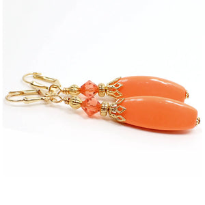 Side view of the handmade drop earrings. The metal is gold plated in color. There are faceted glass crystal orange beads at the top. The bottom beads are vintage lucite, are salmon orange in color, and are oval shaped with flat sides.