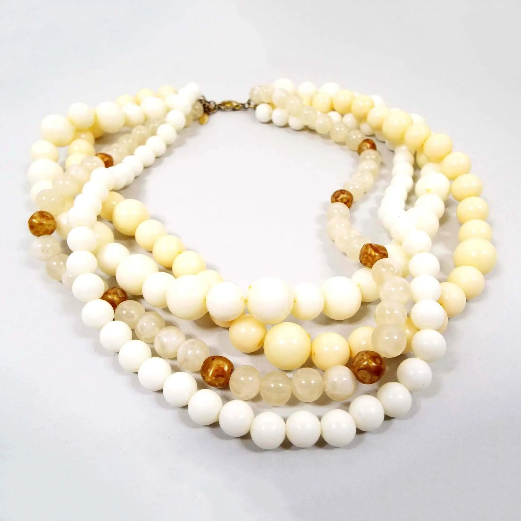 Front view of the retro vintage EsMor multi strand necklace. It is beaded with lucite round beads in white, cream, light yellow, and a marbled golden color.