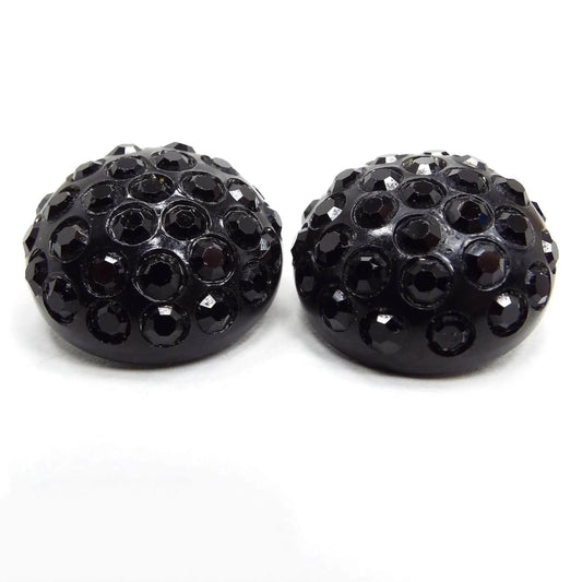 Front view of the Mid Century vintage black rhinestone earrings. They are round in shape with small round black rhinestones and a black plastic setting.