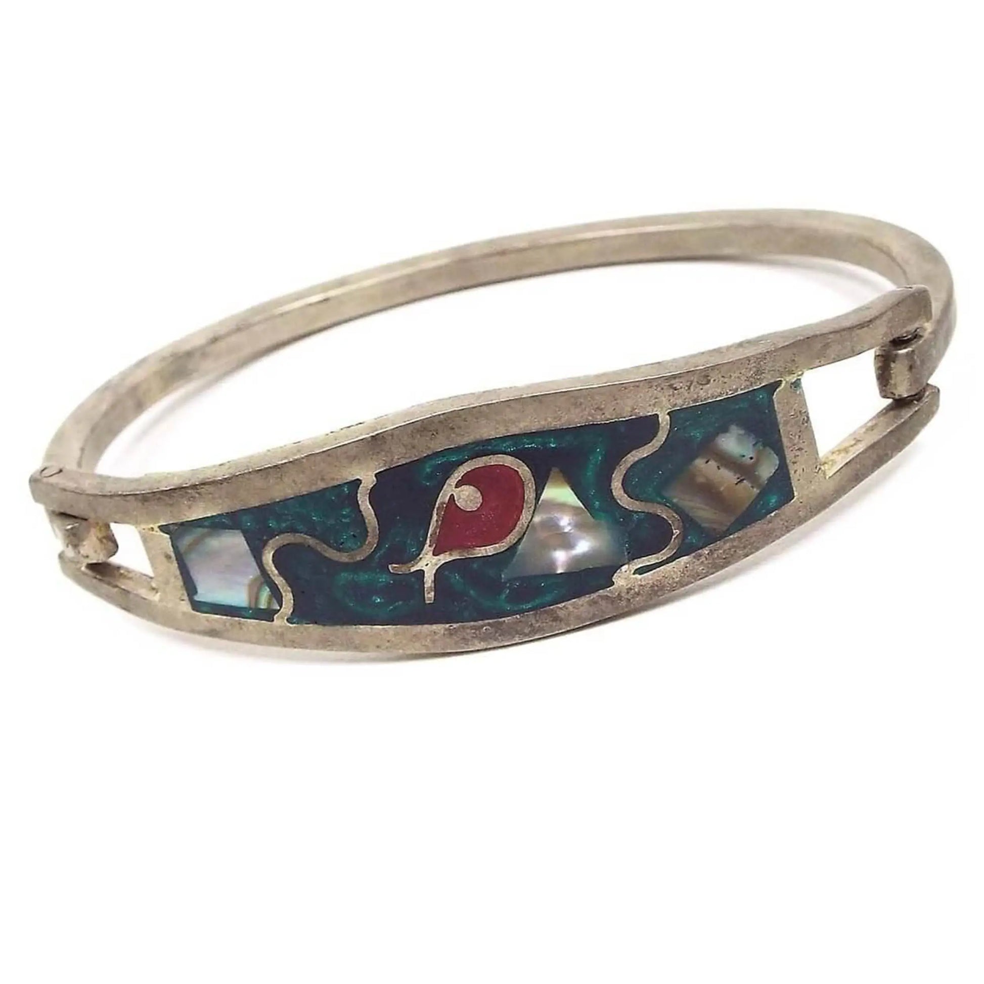 Front view of the Mexican vintage hinged bangle bracelet. It is silver tone in color and has a dark pearly green enamel on the front. There is a small red enameled fish and three pieces of inlaid abalone shell in the design.