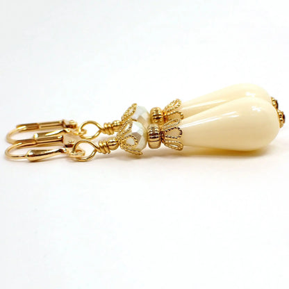 Side view of the handmade lucite beaded teardrop earrings. The metal is gold plated in color. There is a faceted off white glass bead at the top. The bottom bead is a vintage lucite teardrop shaped bead in an off white cream color.