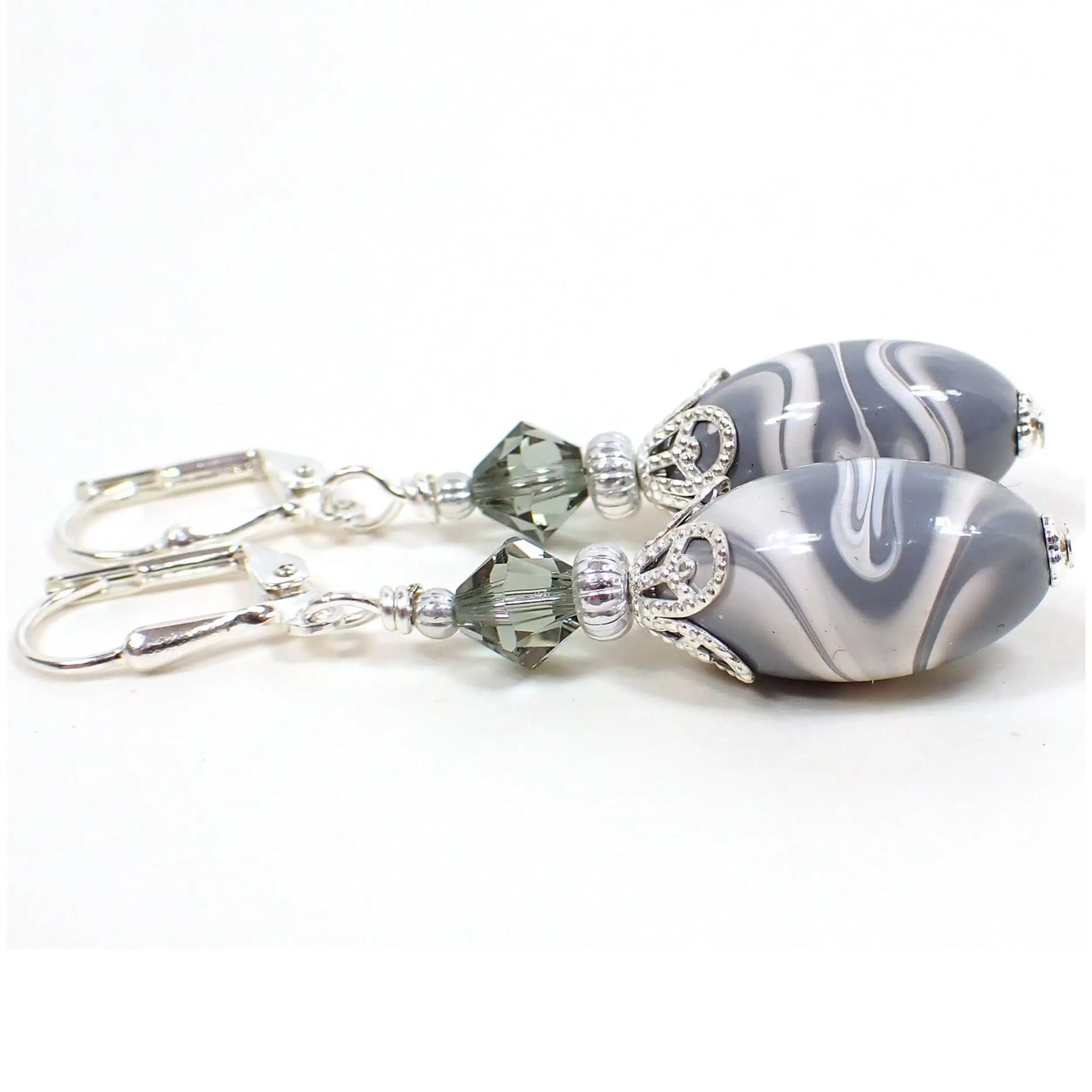 Side view of the handmade earrings with vintage lucite beads. The metal is silver plated in color. There are faceted glass crystal beads in smoky gray at the top. The bottom lucite beads have marbled swirls of bluish gray and white. Each bottom bead is different in pattern from the other for a unique appearance.