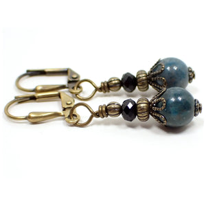 Enlarged side view of the small handmade apatite drop earrings. The metal is antiqued brass in color. There is a faceted glass crystal rondelle bead at the top and a small round ball apatite gemstone bead at the bottom. The gemstone is a marbled teal blue in color.