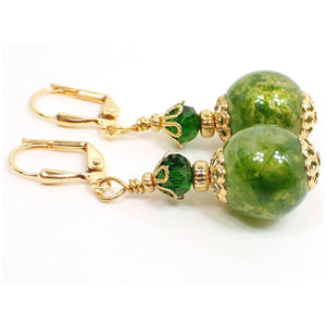 Side view of the handmade acrylic drop earrings. The metal is gold plated in color. There are faceted glass crystal oval beads in grass green at the top of the earrings. The bottom acrylic beads have marbled swirls of lighter shades of green and a light metallic golden sheen.