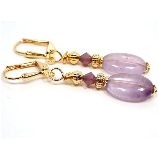 Side view of the handmade amethyst earrings. The metal is gold plated in color. There are faceted glass crystal beads at the top in a semi transparent purple color. The bottom gemstone beads are a light purple with some small areas of darker purple mixed in.
