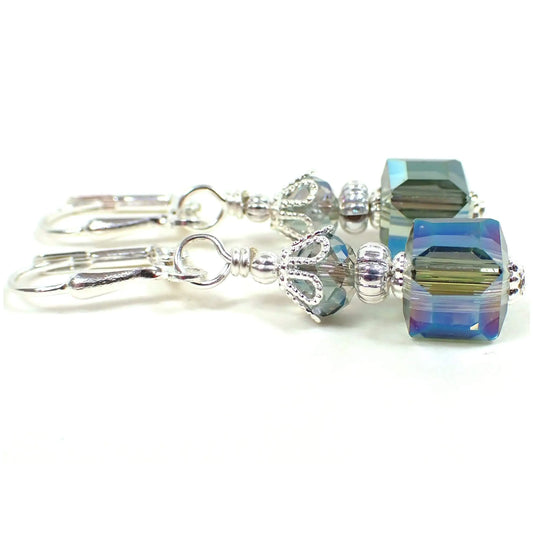 Side view of the handmade small cube earrings. The metal is silver plated in color. There are faceted glass crystal rondelle beads at the top and square cube beads at the bottom. The beads are a mix of green and blue with an AB coating that has small flashes of other colors as you move around in the light.