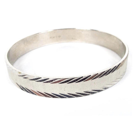 Front view of the retro vintage Monet bangle bracelet. The metal is silver tone in color and it has a textured thin line design. There are faceted angled etched edges.