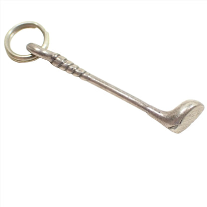 Enlarged angled view of the small golf club charm. It is light pewter gray in color and is shaped like a golf club with a small spit jump ring at the top.