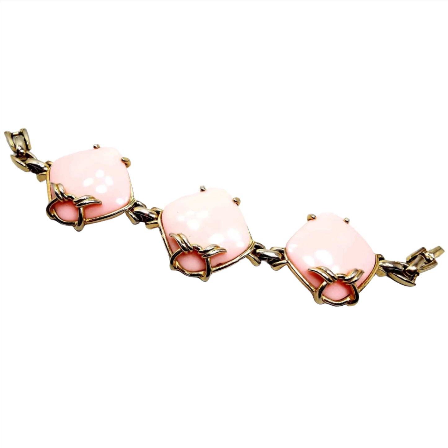 Top view of the Mid Century vintage link bracelet. The metal is gold tone in color. There are three large puffy style diamond shaped cabs in the middle that are light pink in color and made of plastic. There is a snap lock clasp at the end.