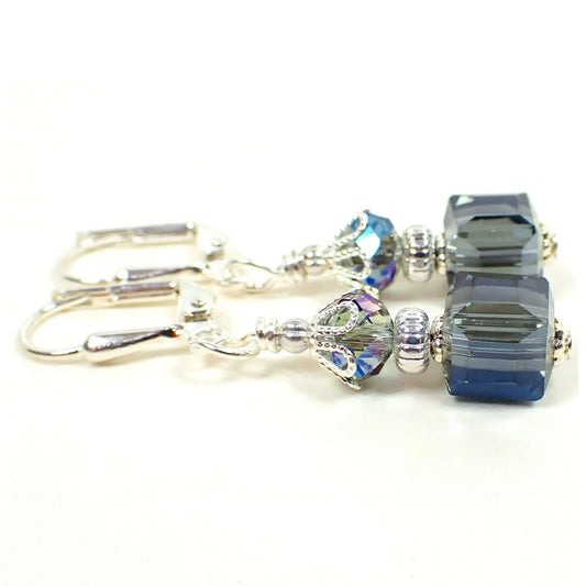 Side view of the small handmade cube earrings. The metal is silver plated in color. There are faceted glass crystal rondelle beads at the top and square cube beads at the bottom. The beads have a smokey blue color with vibrant blue accents.