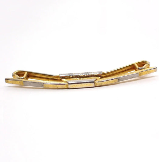 Enlarged front view of the 1920's Swank B&W Plate vintage collar clip. The clip is mostly gold tone plated in color. The front has a step like appearance with a silver tone area in the middle of each side. The gold tone areas on the front have tiny thin etched lines. The side is marked B&W Plate and with a patent number 75818.