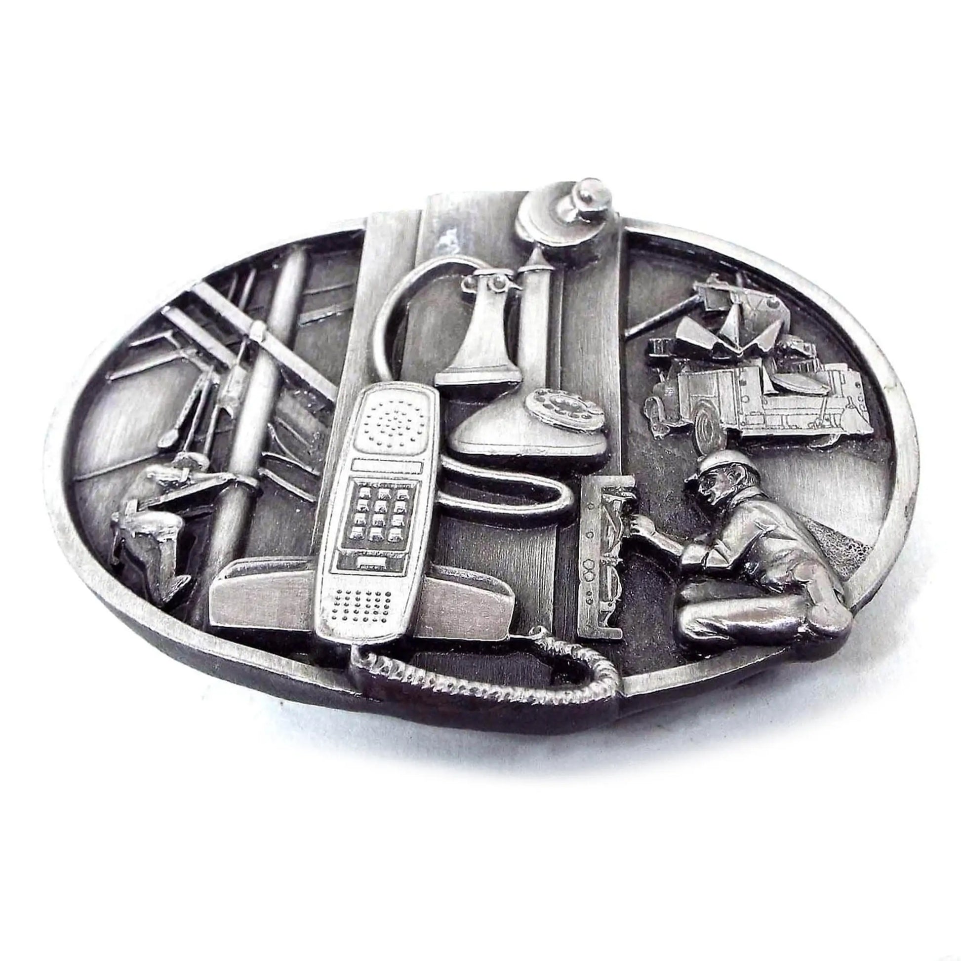 Front view of the retro vintage Sikiyou telecommunications belt buckle. It has a depiction of two old phones on the front and telecommunications workers. It is pewter gray in color.