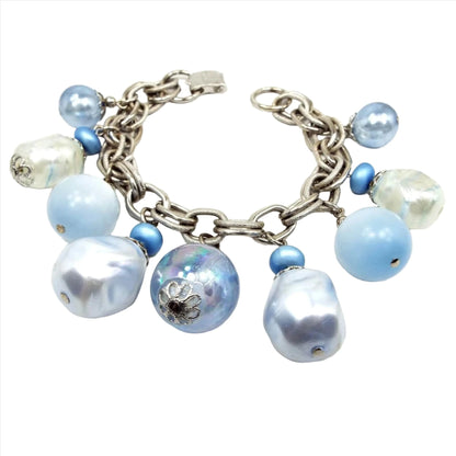Angled top view of the Mid Century vintage beaded chain bracelet. The chain is silver tone in color with textured double cable links. It has varying large beads in pearly white, moonglow lucite blue, a shimmery metallic like blue, and AB blue.