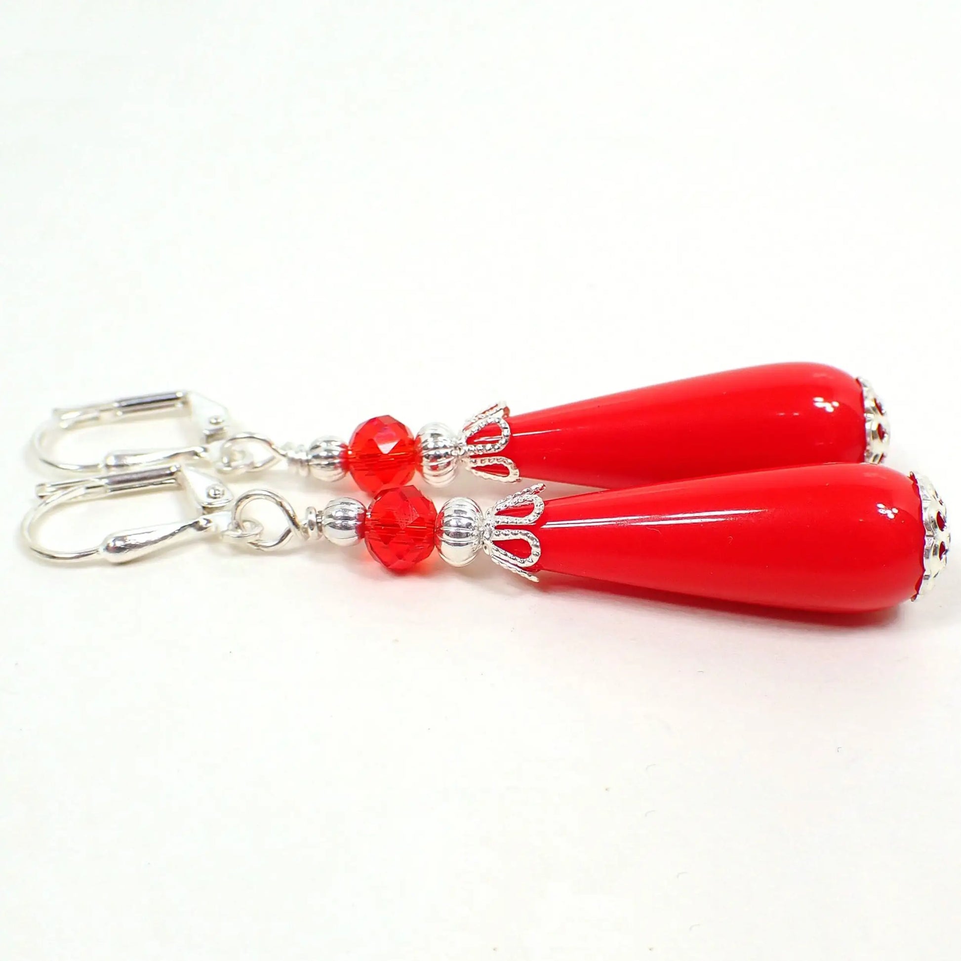 Side view of the handmade teardrop earrings with vintage lucite beads. The metal is silver plated in color. There are new faceted glass crystal beads in red at the top. The bottom lucite beads are bright red and teardrop shaped.