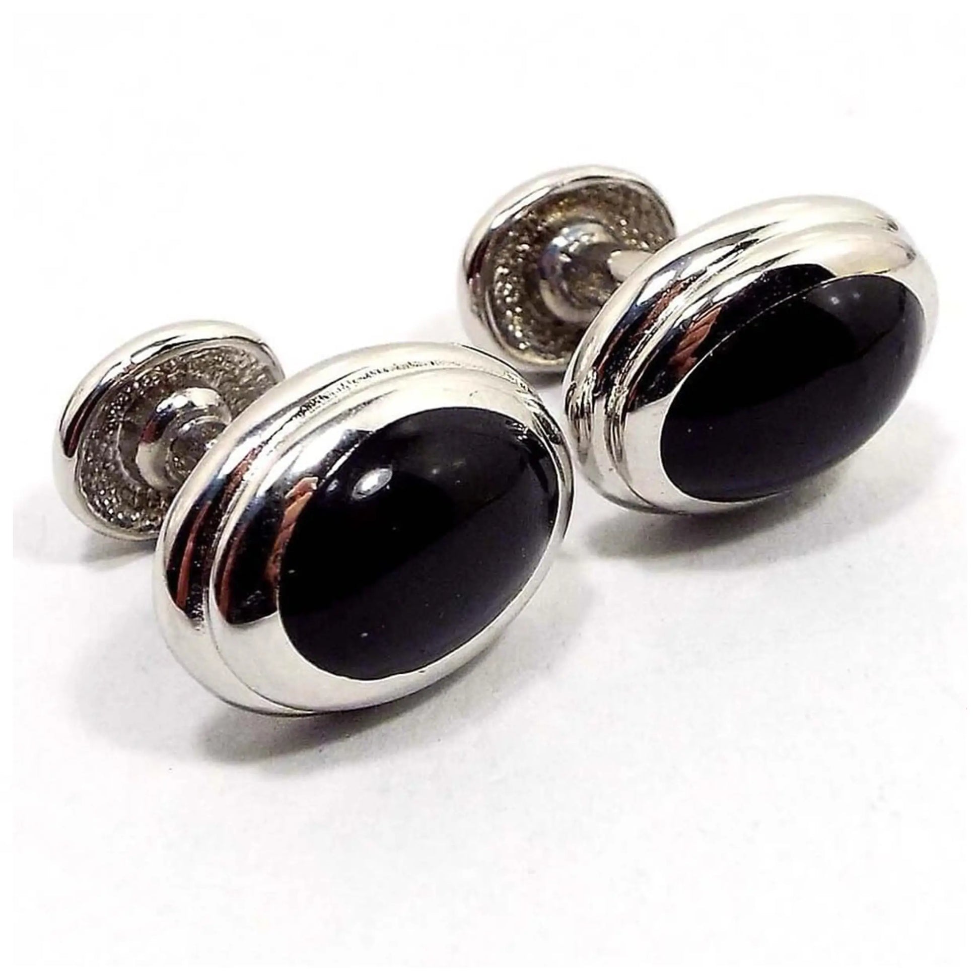 Angled view of the Mid Century vintage bean back cufflinks. The metal is gold tone in color. They are oval in shape and have black plastic fronts.