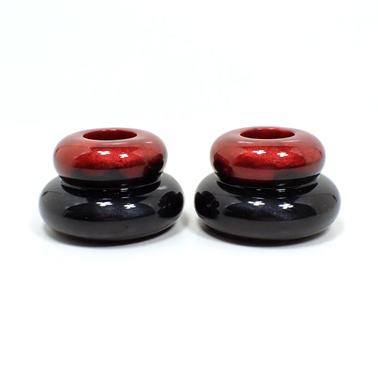 Side view of the handmade resin double ring candlestick holders. They are shaped like puffy donut rings with a smaller one on top and larger one on the bottom. The red resin is on the top of the piece and goes down into the black resin on the bottom.