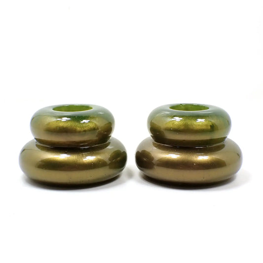 Side view of the handmade resin double ring candlestick holders. They are shaped like puffy donut rings with a smaller one on top and larger one on the bottom. The resin has shades of green, olive green, metallic gold, and golden brown. 