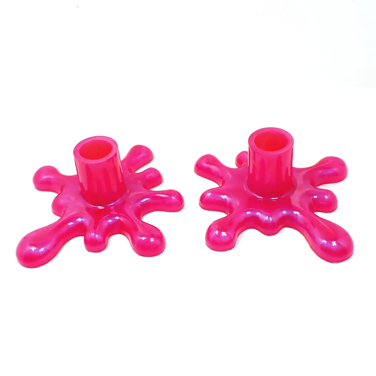 Angled view of the handmade resin larger sized splat style candlestick holders. They are bright pearly pink in color. The top part that holds the candle is round tube shaped. The bottom has a splat drip style design that is asymmetrical and has rounded ends. 