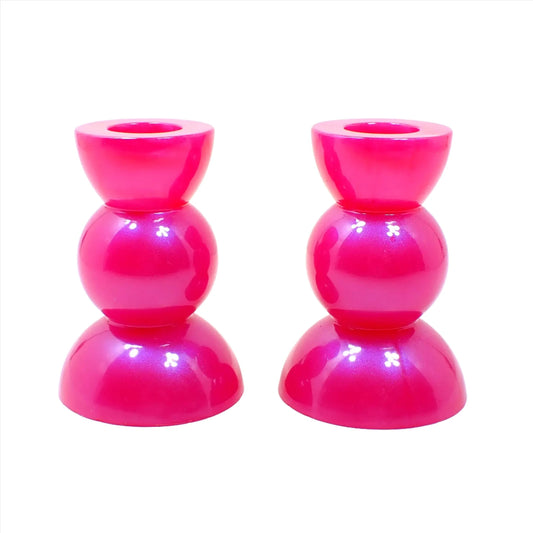 Side view of the handmade bright pink resin rounded geometric candlestick holders. They are bright pearly pink in color. They are shaped with a semi circle at the top and bottom with a sphere shape in between.