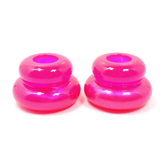 Side view of the pair of handmade double ring candlestick holders. They are shaped like puffy donut rings with a larger one on bottom and a smaller one on top. The resin is bright pearly pink towards the bottom and bright neon pink towards the top. There is a round hole at the top for the candlesticks to go in.