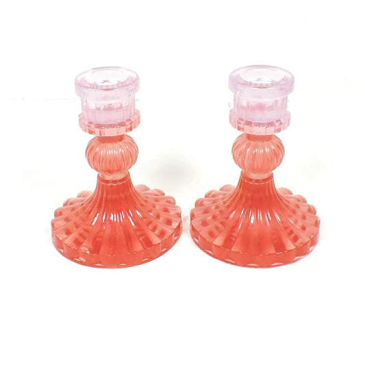 Side view of the vintage style handmade resin candlestick holders. They have a round cylinder style shape at the top, a corrugated round middle, and a flared out bottom with a corrugated ripple design. The resin is translucent purple at the top and translucent red at the bottom.
