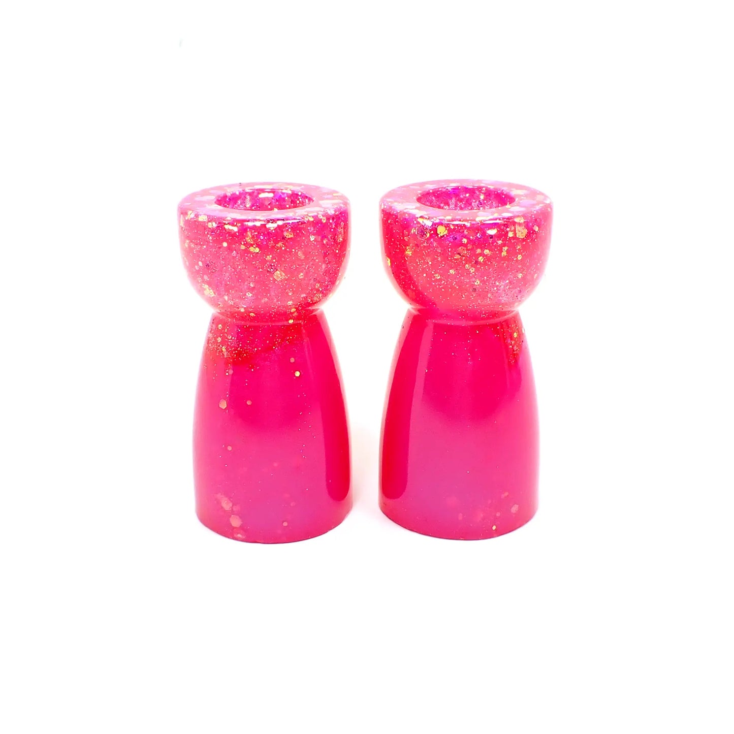 Side view of the handmade resin candlestick holders. They have bright pearly pink resin and chunky iridescent glitter. The glitter shows mostly at the top portion of the pieces. They are rounded on top and a cone like shape underneath that flares out to the bottom.