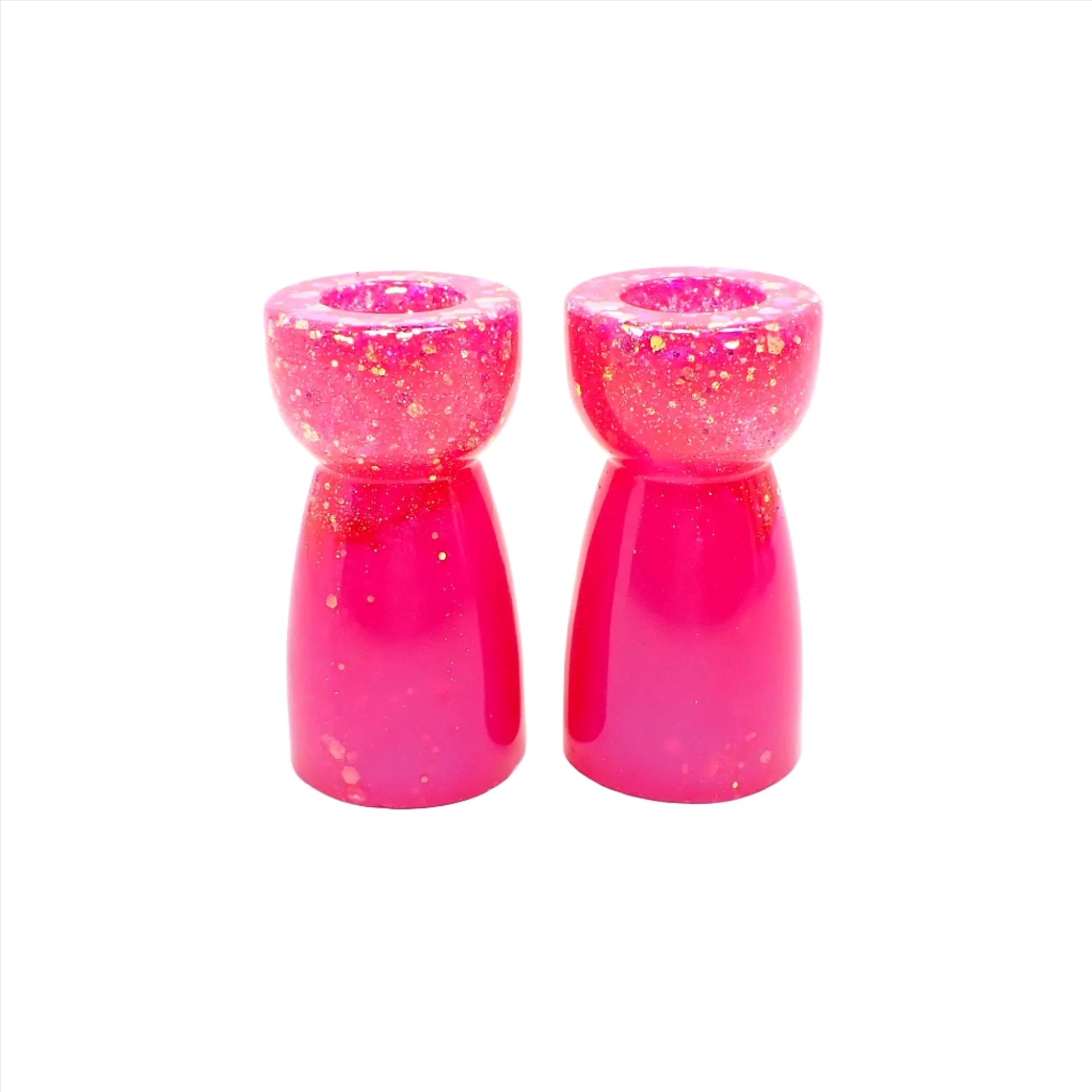 Side view of the handmade resin candlestick holders. They have bright pearly pink resin and chunky iridescent glitter. The glitter shows mostly at the top portion of the pieces. They are rounded on top and a cone like shape underneath that flares out to the bottom.
