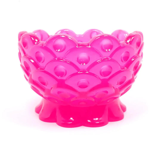 Side view of the handmade resin decorative footed bowl. The resin is bright neon pink in color. It has a scalloped foot and top edge. There is a fish scale like design all the way around the bowl with an indented dot inside each scale area.