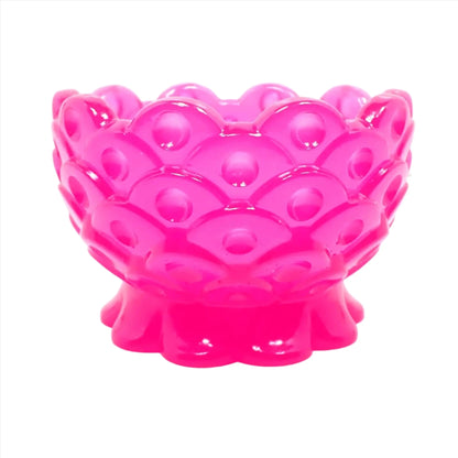 Side view of the handmade resin decorative footed bowl. The resin is bright neon pink in color. It has a scalloped foot and top edge. There is a fish scale like design all the way around the bowl with an indented dot inside each scale area.
