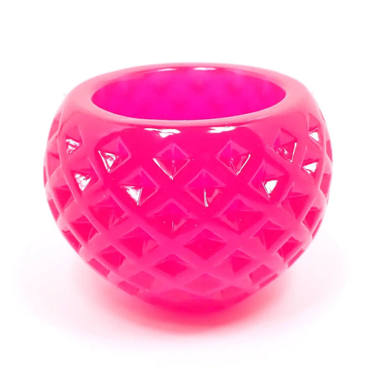 Side view of the small round handmade resin succulent pot. The resin is bright neon pink in color. There is a diamond shaped indented pattern all the way around it. The top has a round opening for tiny plants or small trinkets.