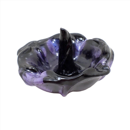 Angled view of the handmade resin ring dish holder. It's shaped like a flower with the petals open and one in the middle sticking up for the rings to set on. It has pearly black resin with a slight color shift resin marbled in. The color shift resin is mostly purple, but gives flashes of blue as you move around it in brighter settings.