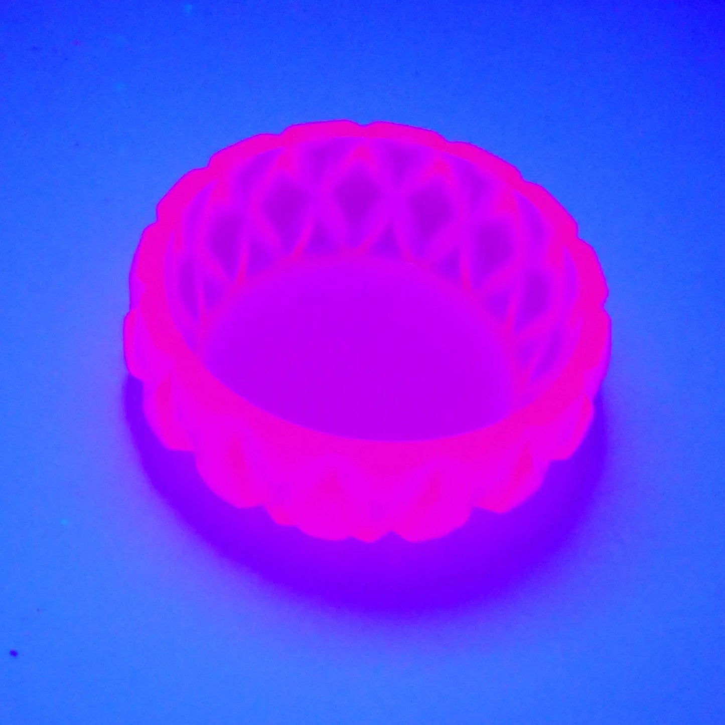 Angled view showing how the small short round handmade succulent bowl trinket dish fluoresces under a UV light in a bright neon pink color. 