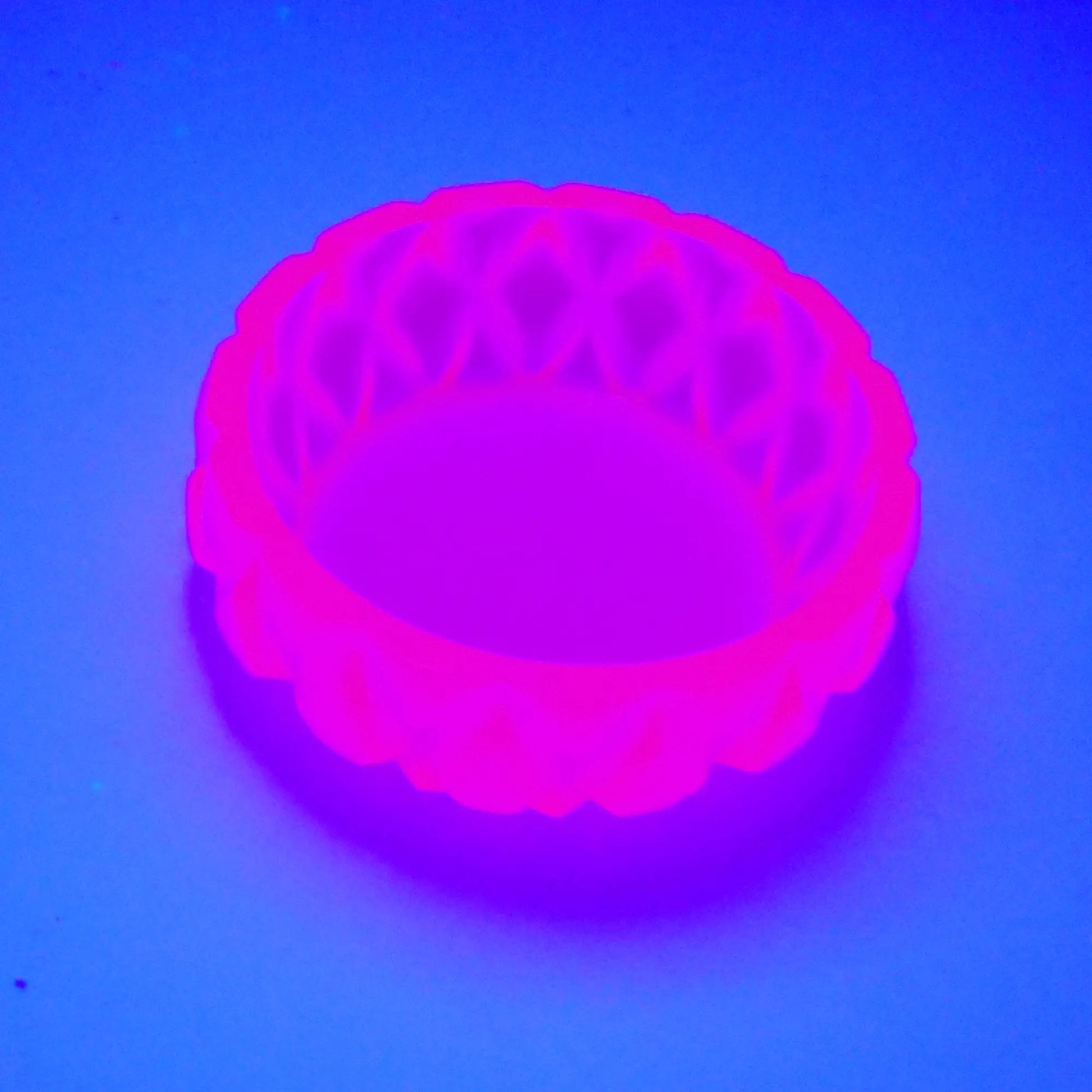 Angled view showing how the small short round handmade succulent bowl trinket dish fluoresces under a UV light in a bright neon pink color. 