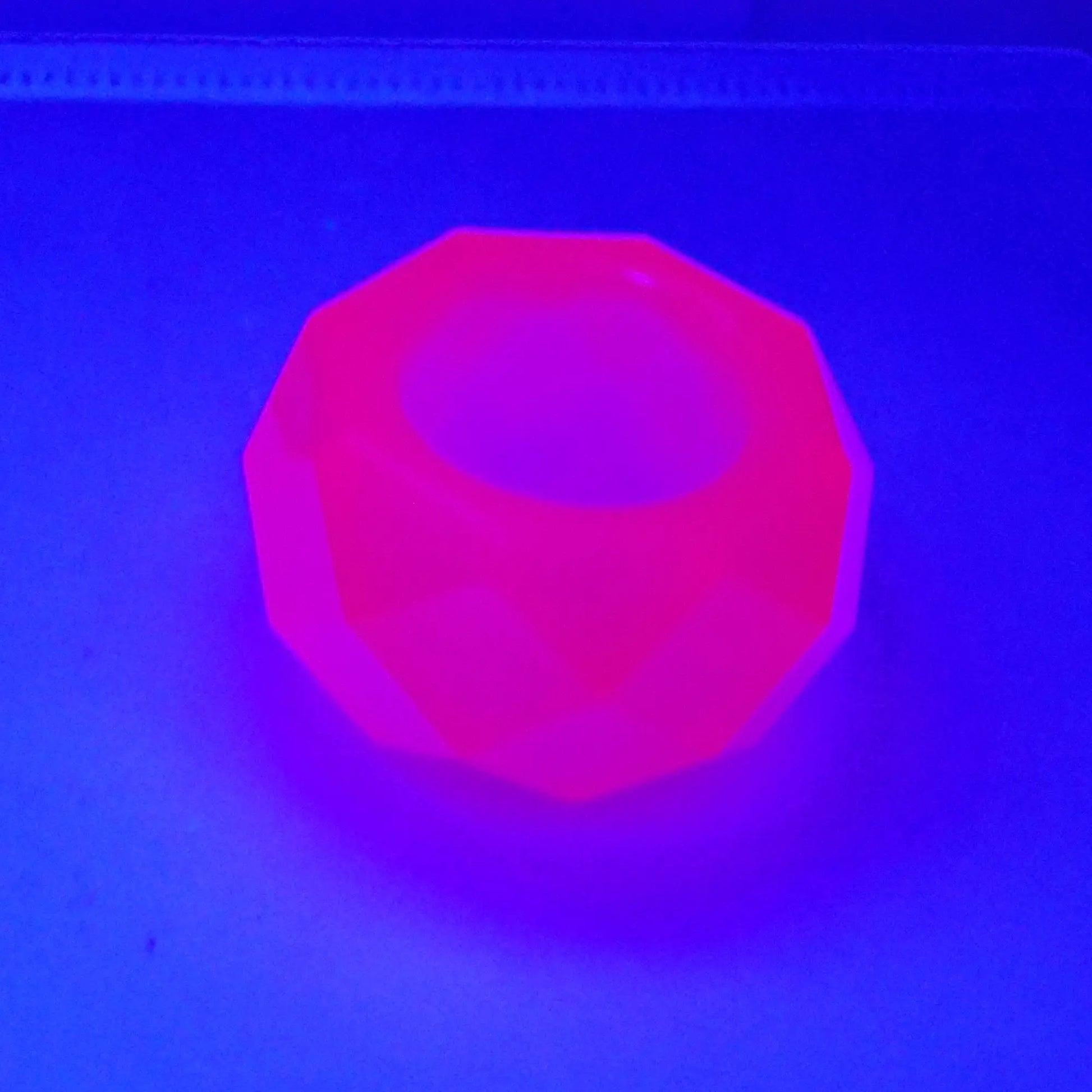 Angled view of the small handmade resin faceted octagon succulent pot showing how it fluoresces bright pink under a UV light. 