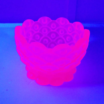 Photo showing the handmade resin decorative footed bowl fluorescing under a UV light. It is a bright neon pink in color.