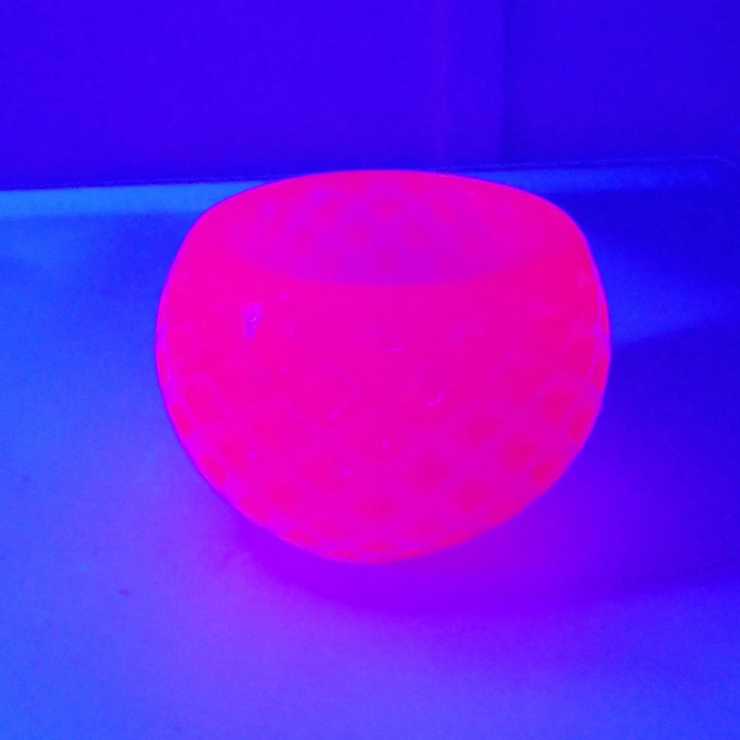 Photo showing how the small handmade neon pink resin succulent pot fluoresces under a UV light in a bright pink color.
