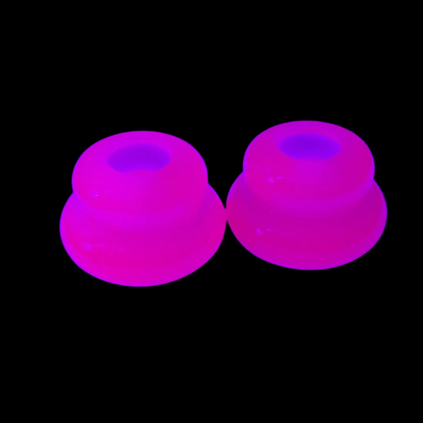 Photo showing how the bright pink handmade resin puffy double ring candlestick holders fluoresce under a UV light. 