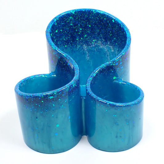 Front view of the handmade resin makeup brush holder. It has pearly aqua blue resin with iridescent glitter at the top. There are three round areas to hold the brushes with the back having the tallest side.